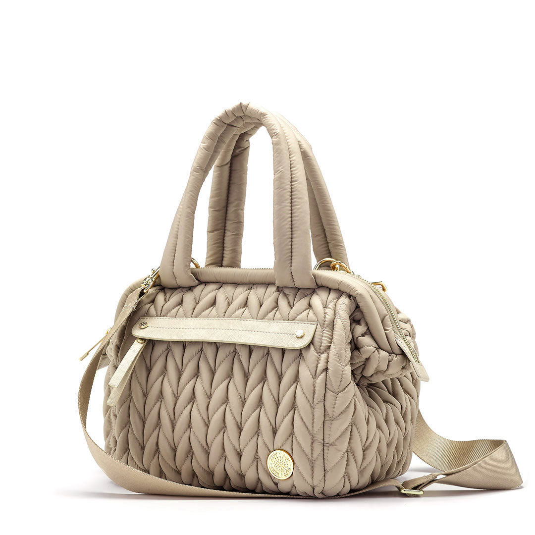 Three-quarters view of the Paige Mini Beige, showing the carry handles, faux-leather-trimmed mommy pocket, and detachable messenger strap.