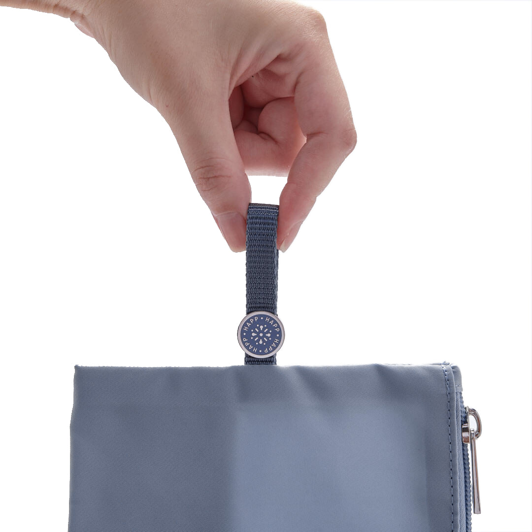 Closeup of a hand holding the blue pull tab found on the Large and Medium pouches, showing off the enamel HAPP logo also in blue.