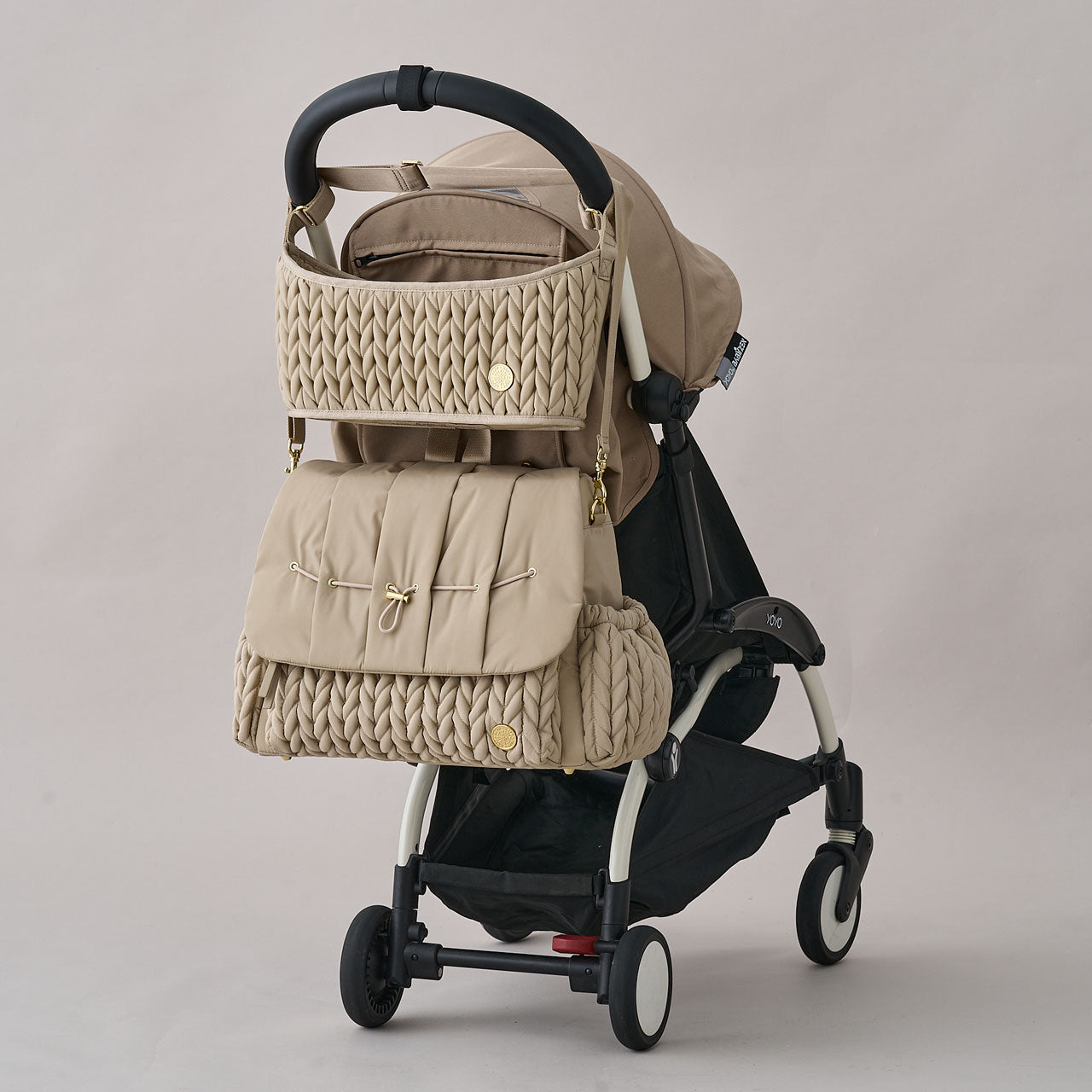 HAPP Stroller Organizer and Levy Backpack in Beige shown attached to a black and beige stroller, with the organizer hanging neatly above the diaper bag.