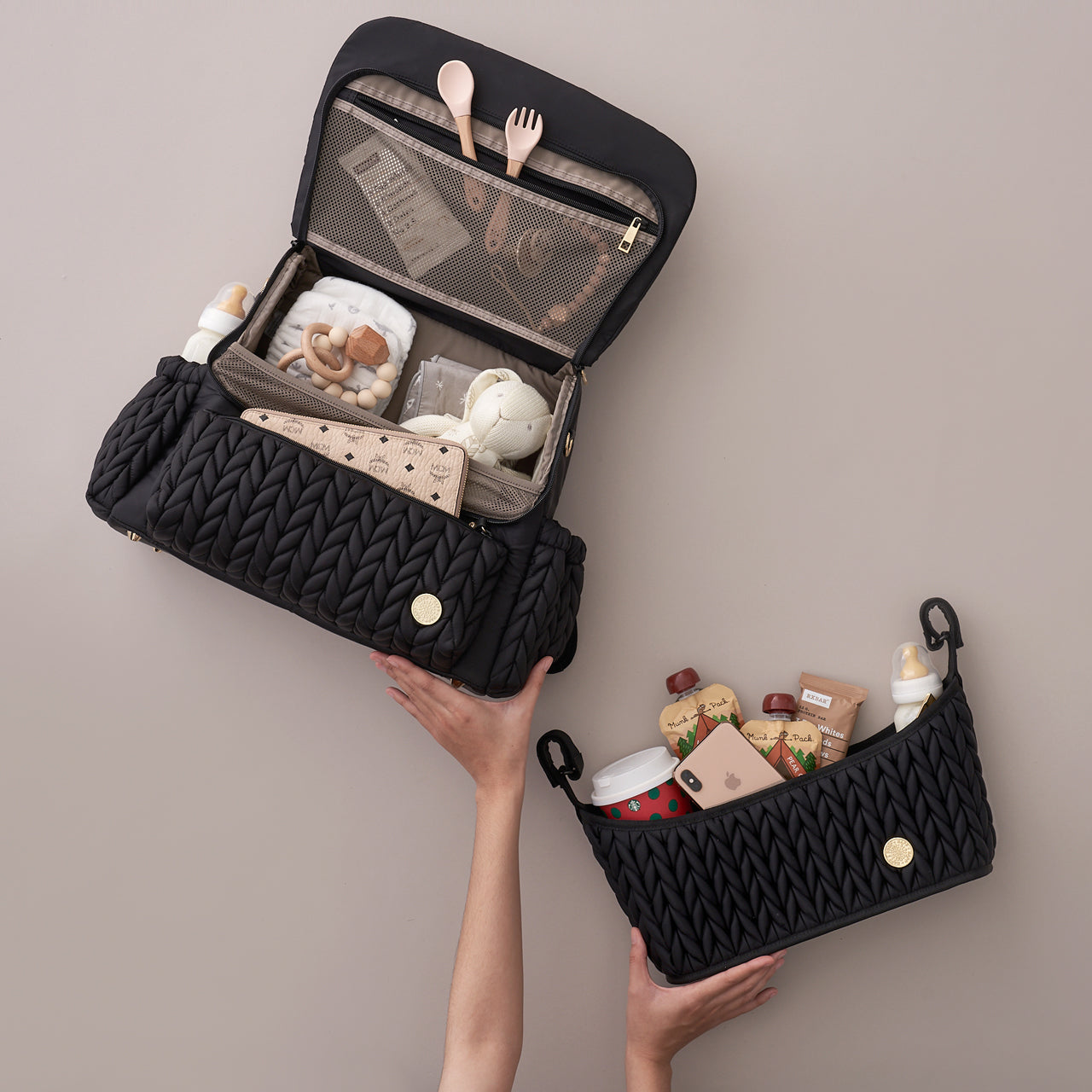 Flat lay of Levy Backpack and Stroller Organizer, both in Black, packed with baby items to show organization, with hands propping them up to show light weight of products.