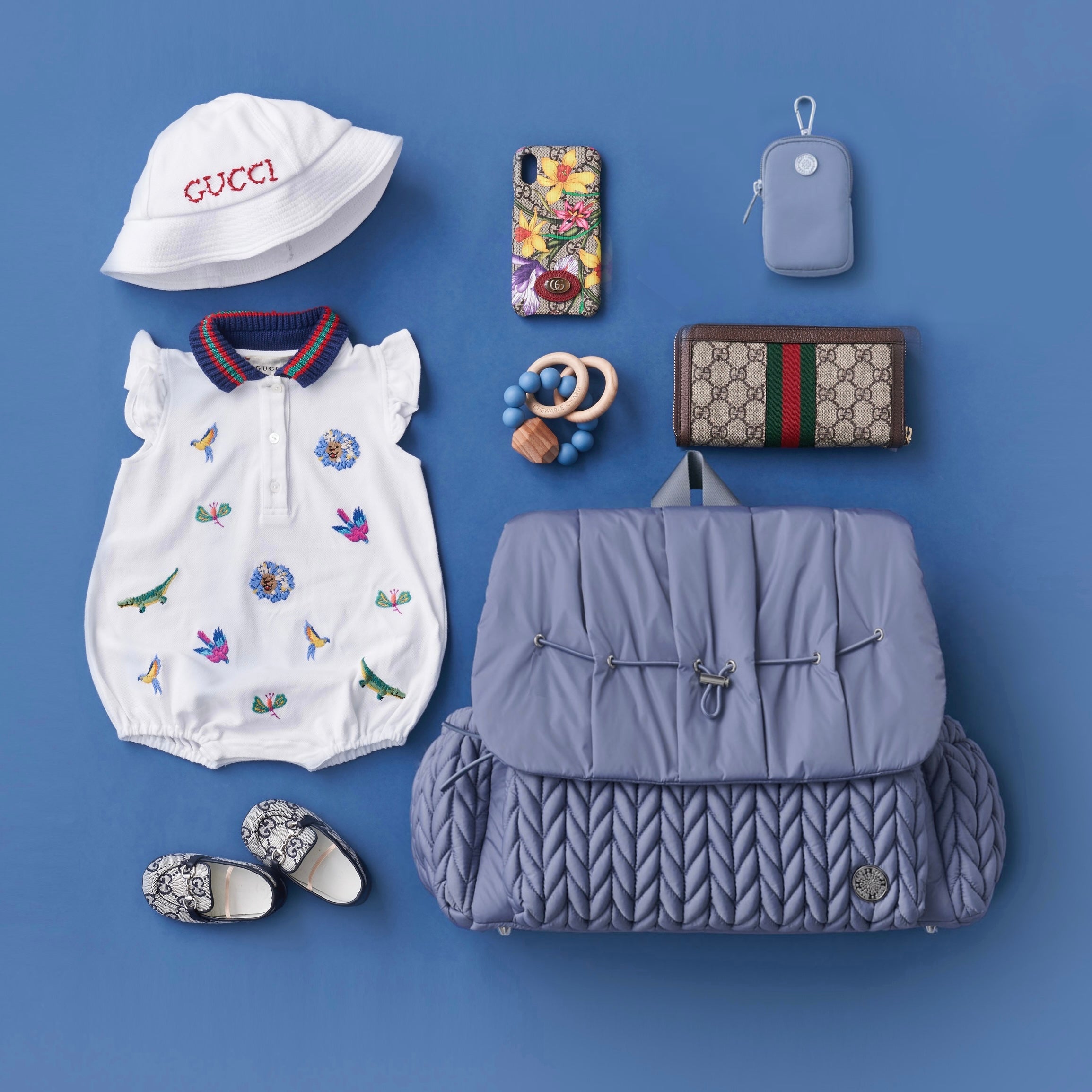 Flat lay of the Levy Backpack in Ash Blue, pictured from the front, arranged with HAPP Clip-on Pouch in Blue and other matching mom and baby items, in a summery theme.