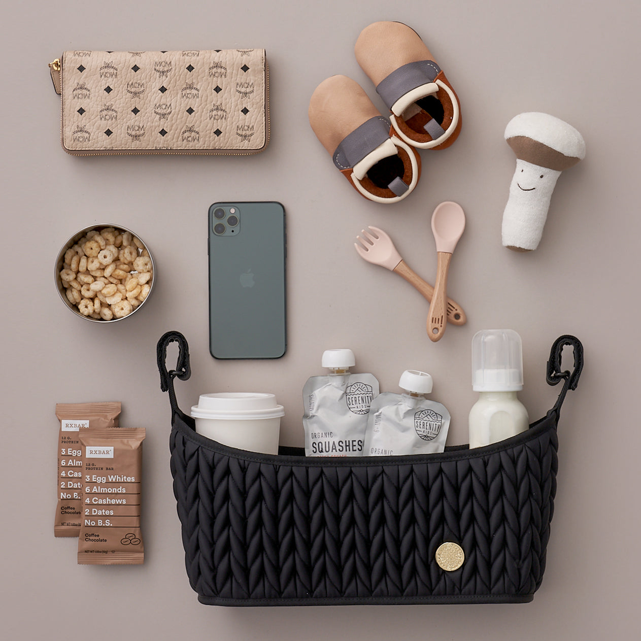 Stroller Organizer in Black lying flat packed with mom and baby items, showing off the quilted herringbone texture, gold hardware detail, and grippy adjustable straps that enable it to attach to almost any stroller.