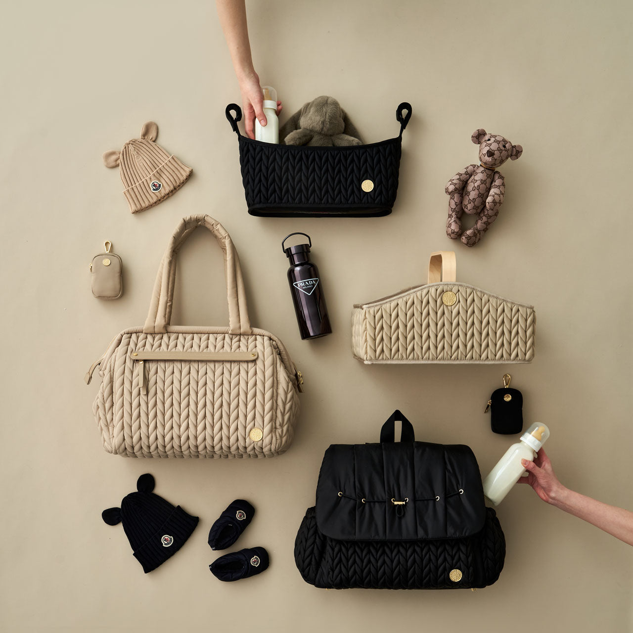 Flat lay of HAPP Neutral collection, showing Levy Backpack Black, Paige Carryall Beige, Stroller Organizer Black, Diaper Caddy Beige, and Clip-on Pouches in both Black and Beige, arranged with matching baby items, with 2 hands taking 1 item out of the organizer and backpack.