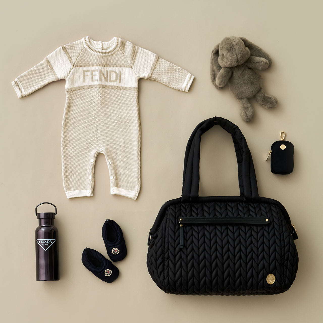 Paige Carryall Black from the front with carry handles upright, next to white and black baby items and a HAPP Clip-on Pouch in Black.