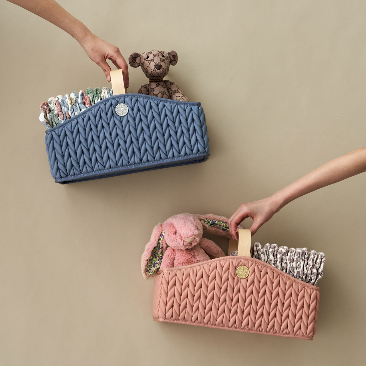 Blue and Rose diaper caddies, packed with matching baby items, each held in one hand, on a beige background.