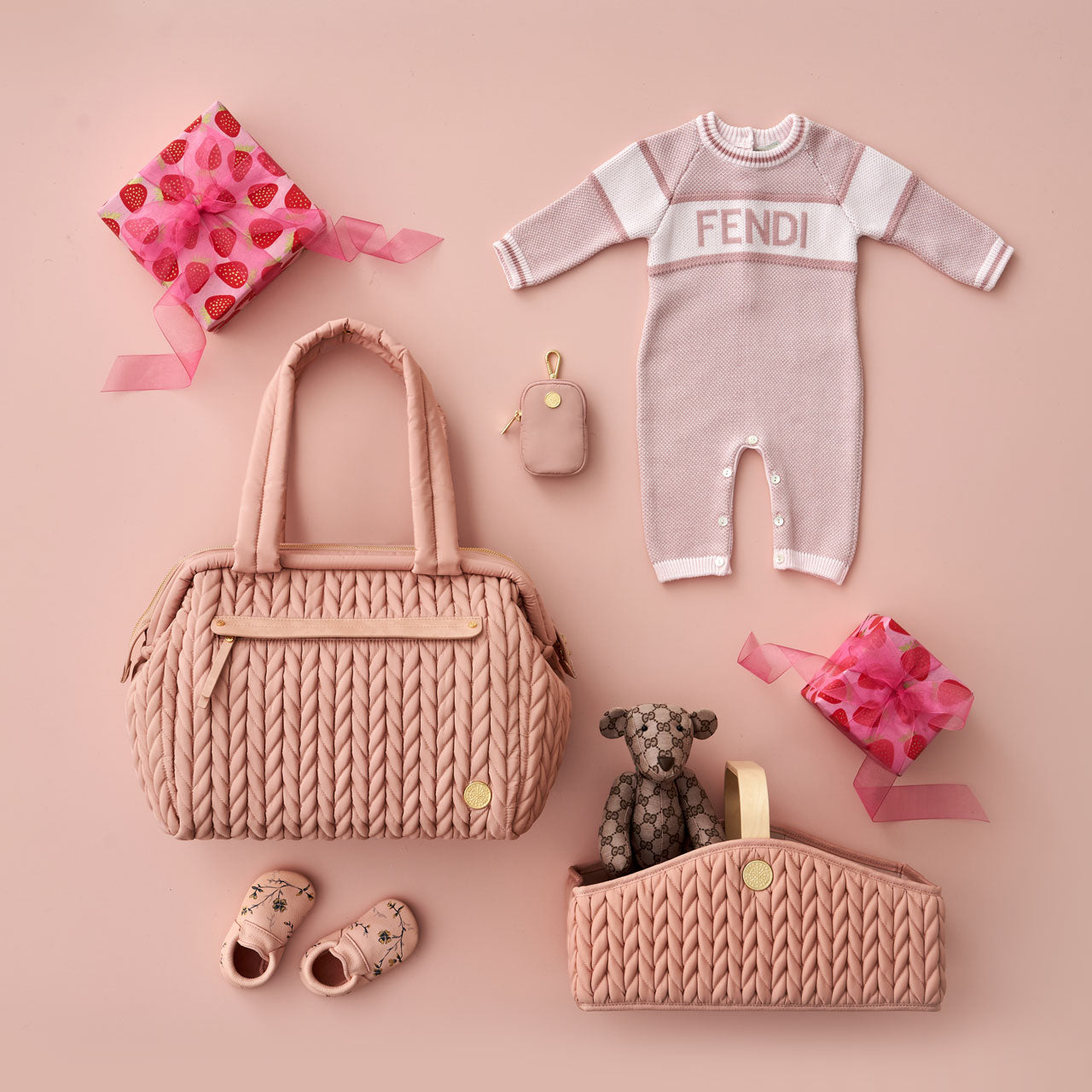 Flat lay with HAPP Paige Carryall and Diaper Caddy in matching rose, on a rose background with rose-pink baby items and two wrapped gifts in a strawberry-pink theme.
