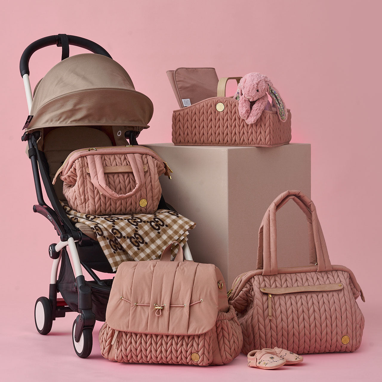 HAPP Dusty Rose collection, including Levy Backpack, Paige Carryall, Paige Mini, and Diaper Caddy, arranged together on and around a baby stroller.