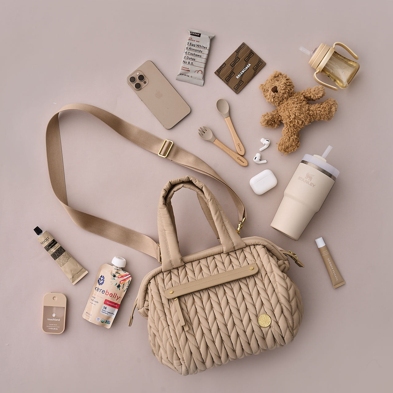 Flat lay of the Paige Mini Beige from the front, showing detachable messenger strap, alongside matching mom and baby items.