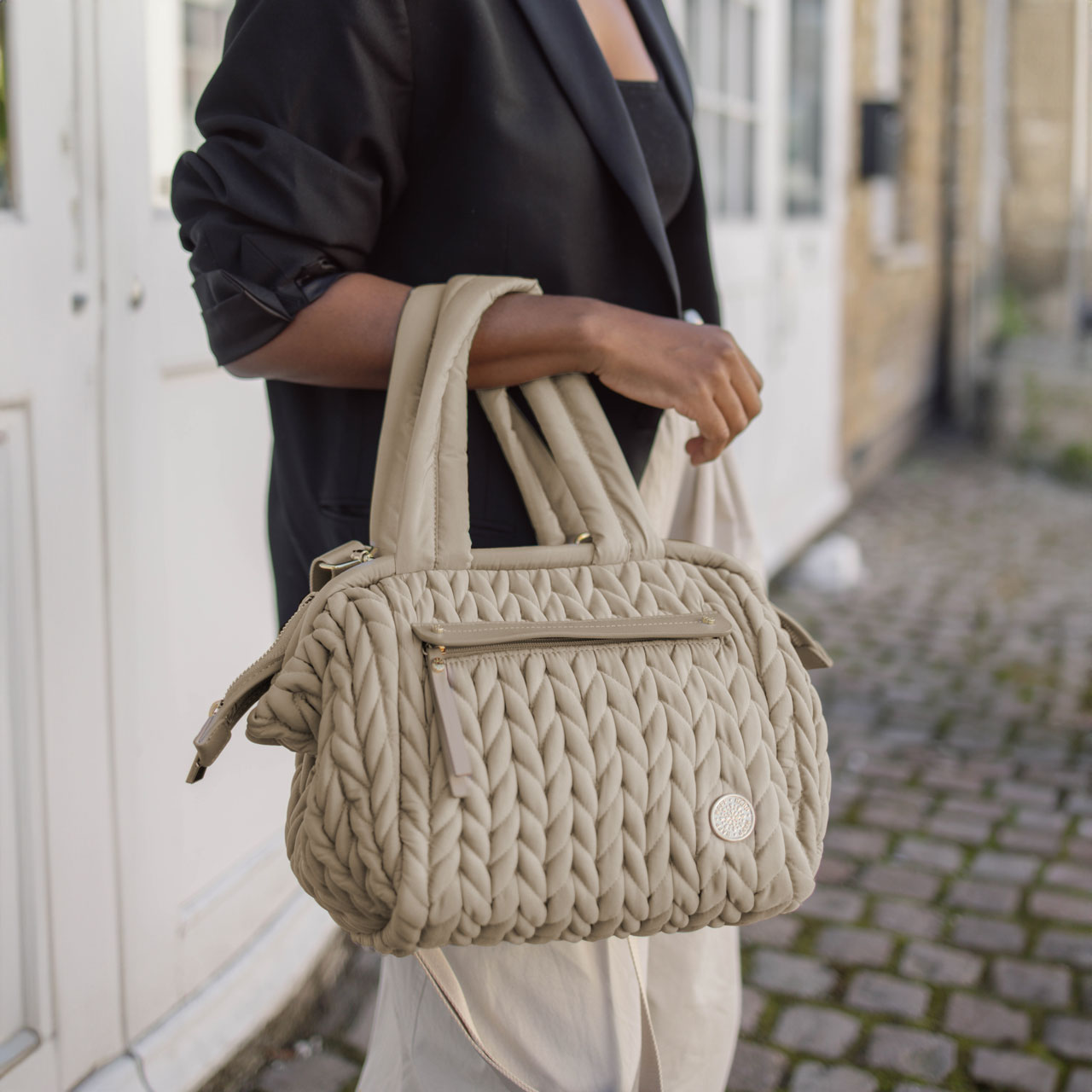 Paige Mini Beige carried by the handles, showing the herringbone quilting and gold hardware details.