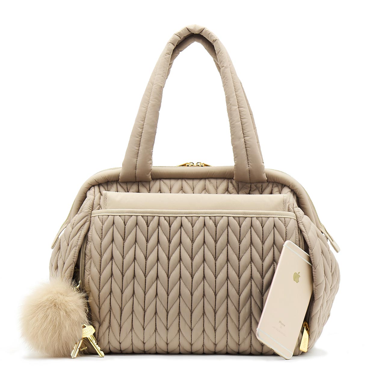 Paige Carryall purse handbag style diaper bag with quilted herringbone nylon in beige with gold hardware with ivory pouf keychain, from the back showing magnet closure changing pad pocket.