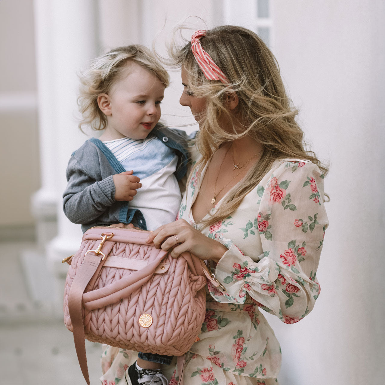 Mom out and about carrying her toddler and a Paige Mini Rose.