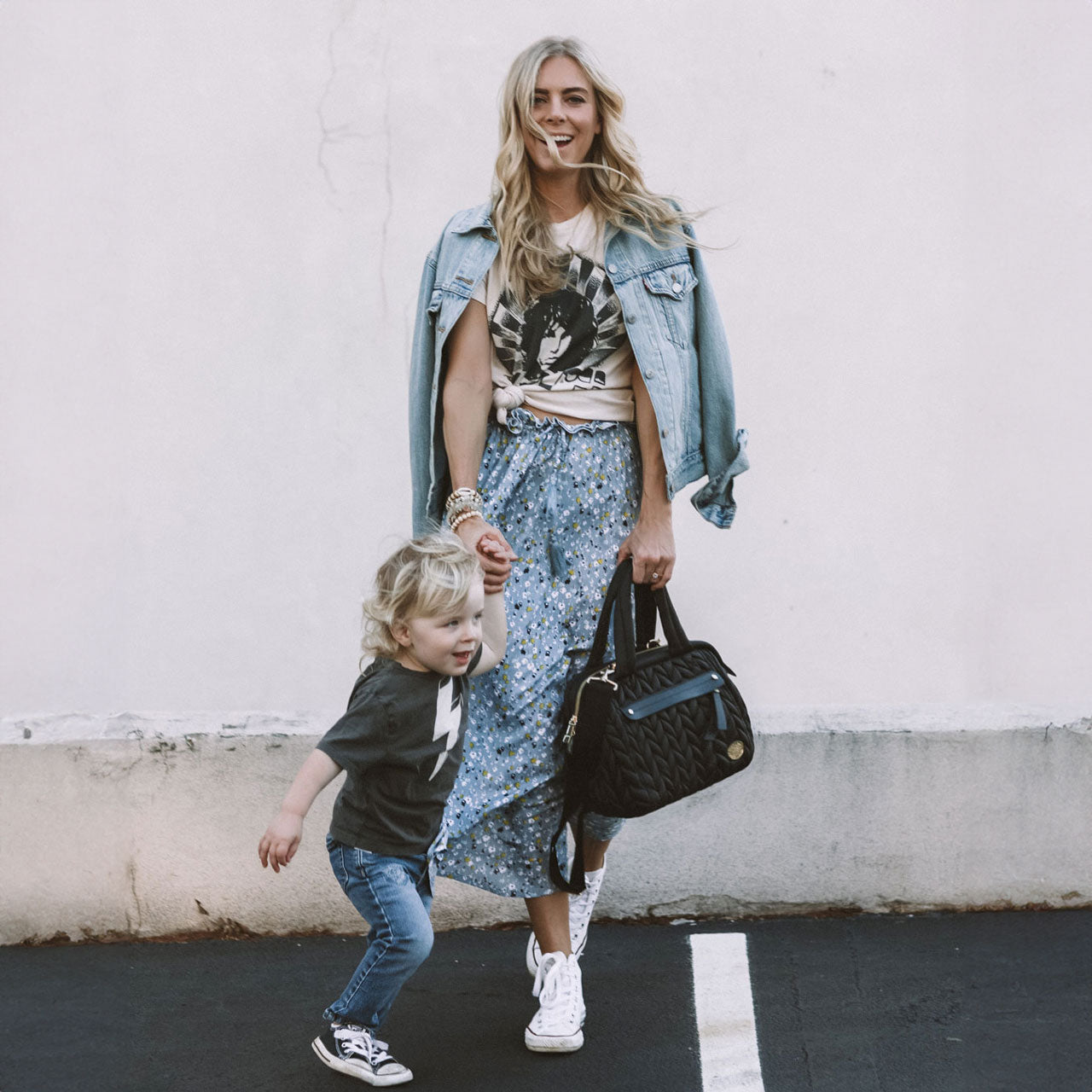 Mom carrying Paige Mini Black by the handles while walking and holding her toddler's hand.