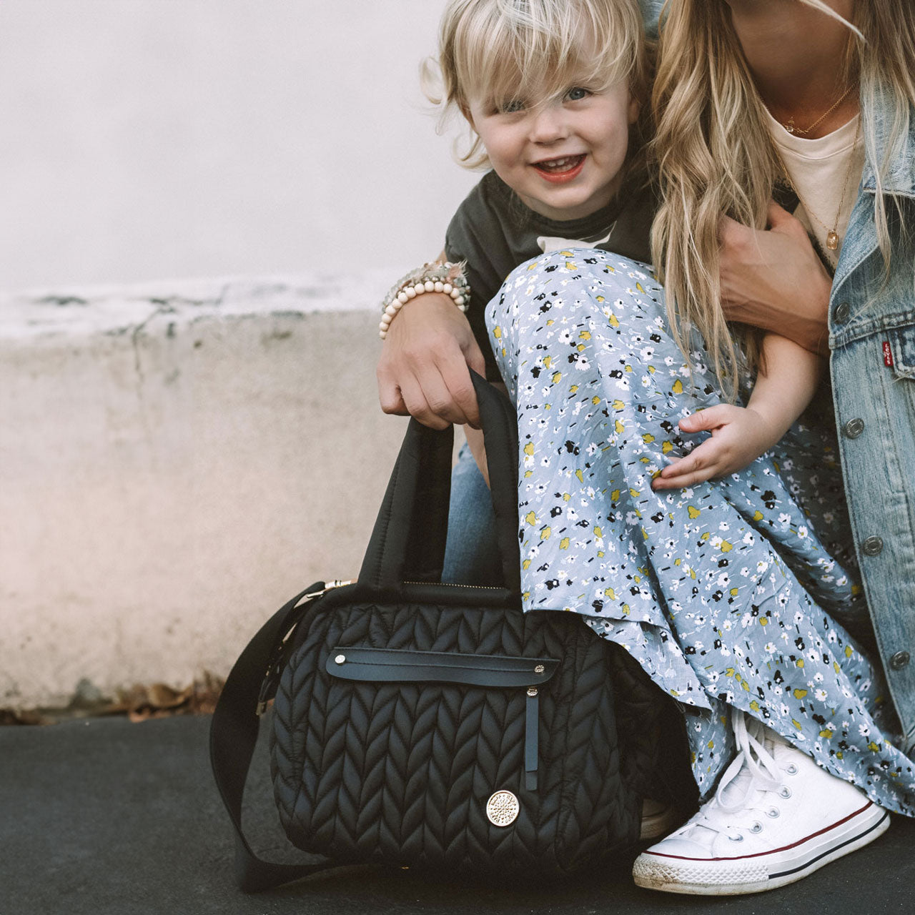 Mom holding mini structured quilted diaper bag by the handles while out and about with her toddler.