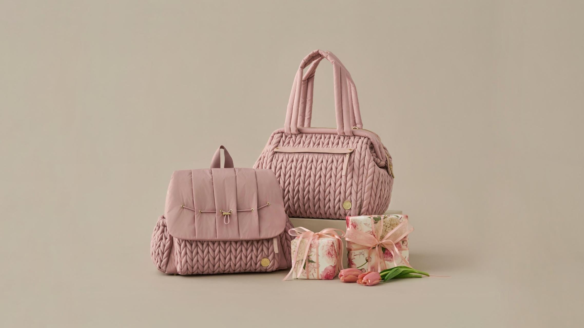 HAPP Brand Levy Backpack and Paige Carryall in signature Dusty Rose herringbone, pictured with two wrapped pink gifts and pink tulips on a beige background.