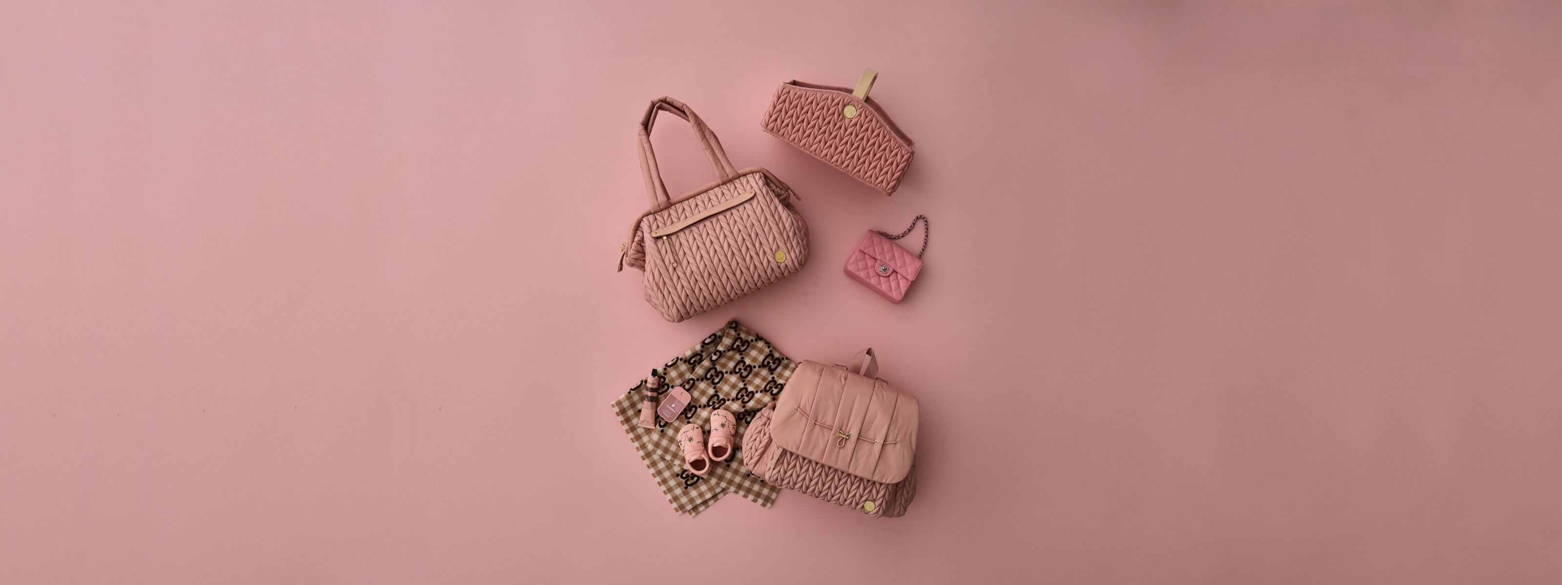 Levy Backpack Dusty Rose, Paige Carryall Dusty Rose, and Diaper Caddy Rose in a flat lay image with matching baby items on a rose background.