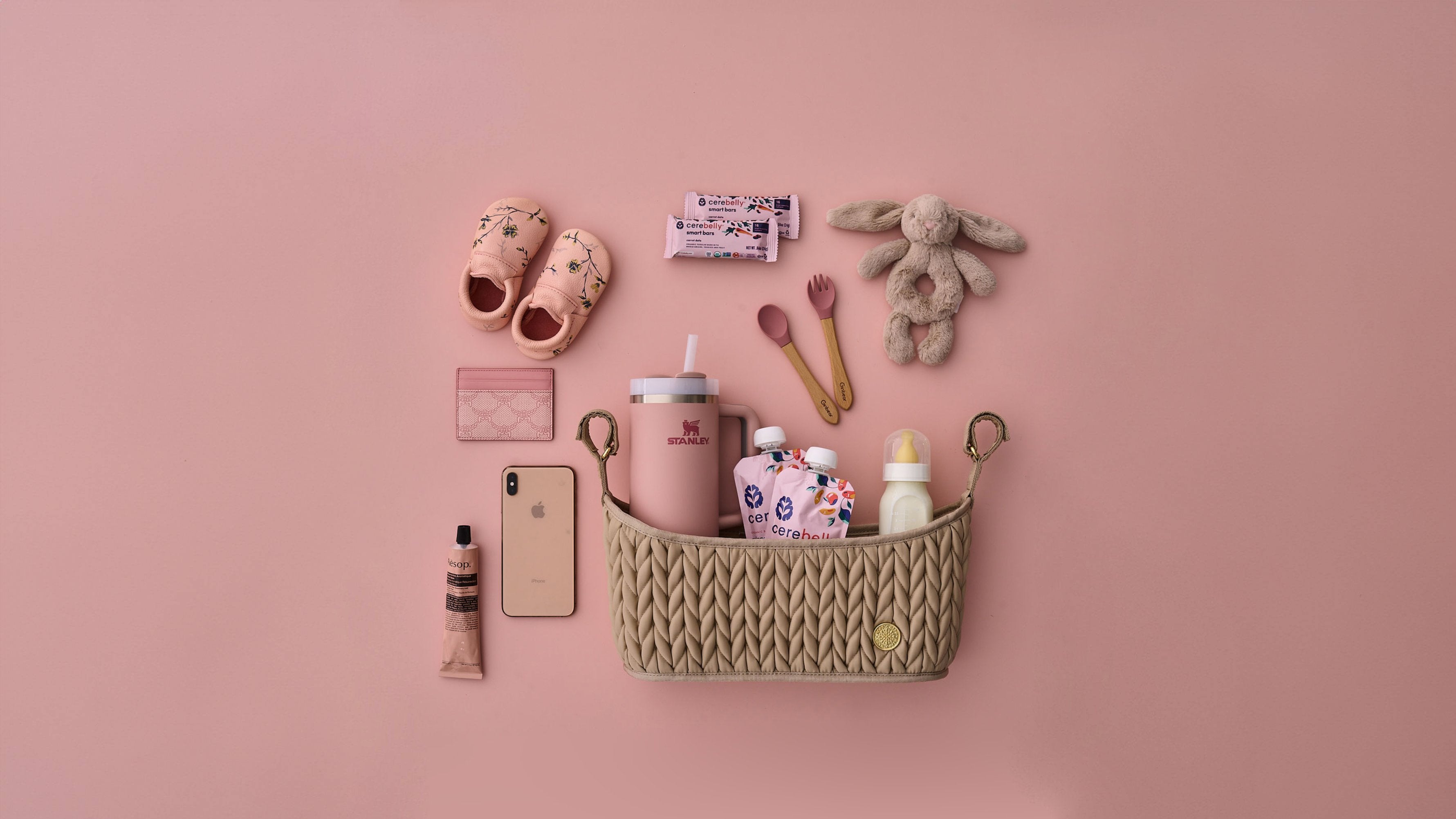 HAPP Brand Stroller Organizer in Beige on a pink background, packed with and surrounded by pink and beige matching baby and mom items.