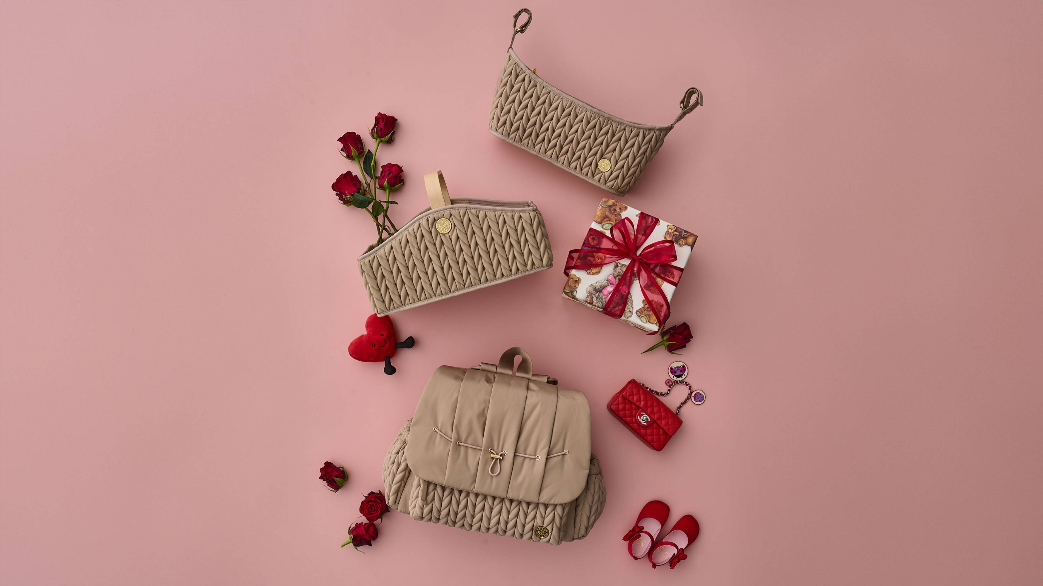 HAPP Brand Beige Herringbone Collection Levy Backpack, Diaper Caddy, and Stroller Organizer on a pink background with red Valentine's Day accessories and red roses.