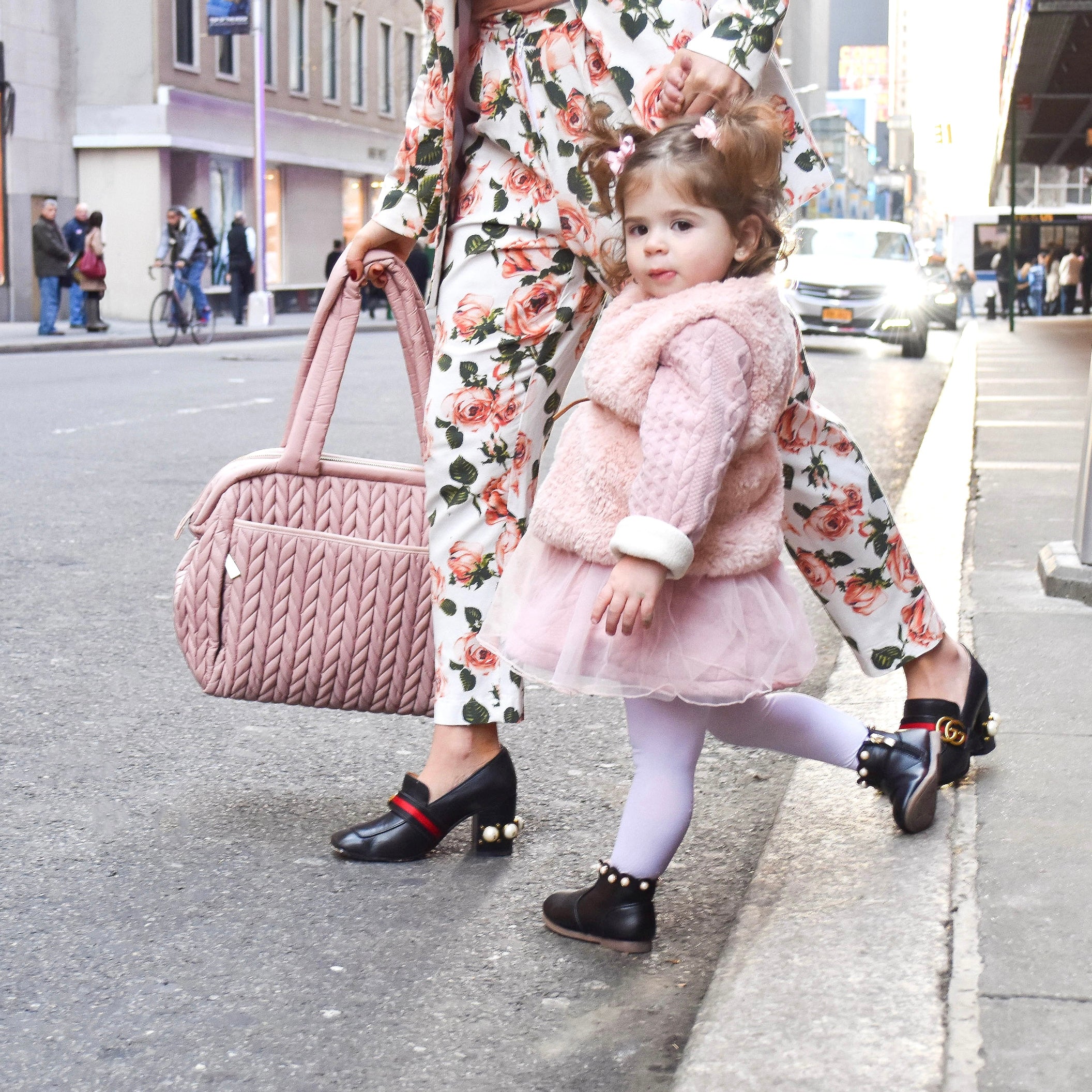 Stylish mom in pink floral pantsuit carrying HAPP Paige Carryall Rose, holding her toddler's hand and crossing the street in NYC.