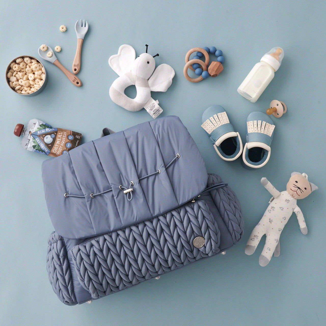 Moving GIF of the Levy Backpack Ash Blue lying flat, with the top flap opening and closing to show the wide-open view and impeccable interior organization of HAPP diaper bags.