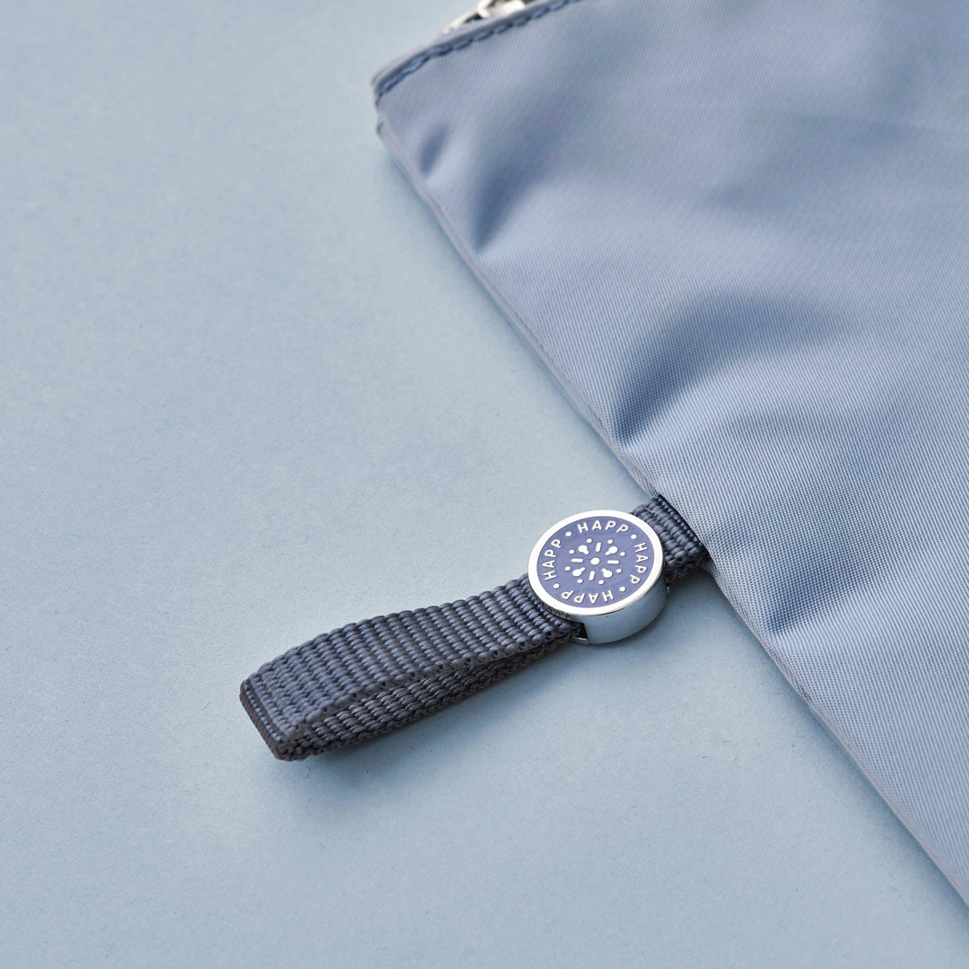 Closeup of the blue pull tab and enamel logo while blue pouch is lying flat on a blue background.