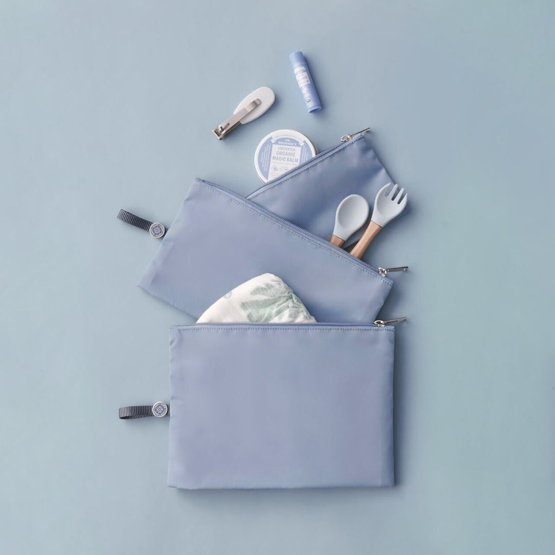 Set of 3 blue packing pouches in varying sizes, laid flat and packed with baby items like diapers, utensils, and hair clips.