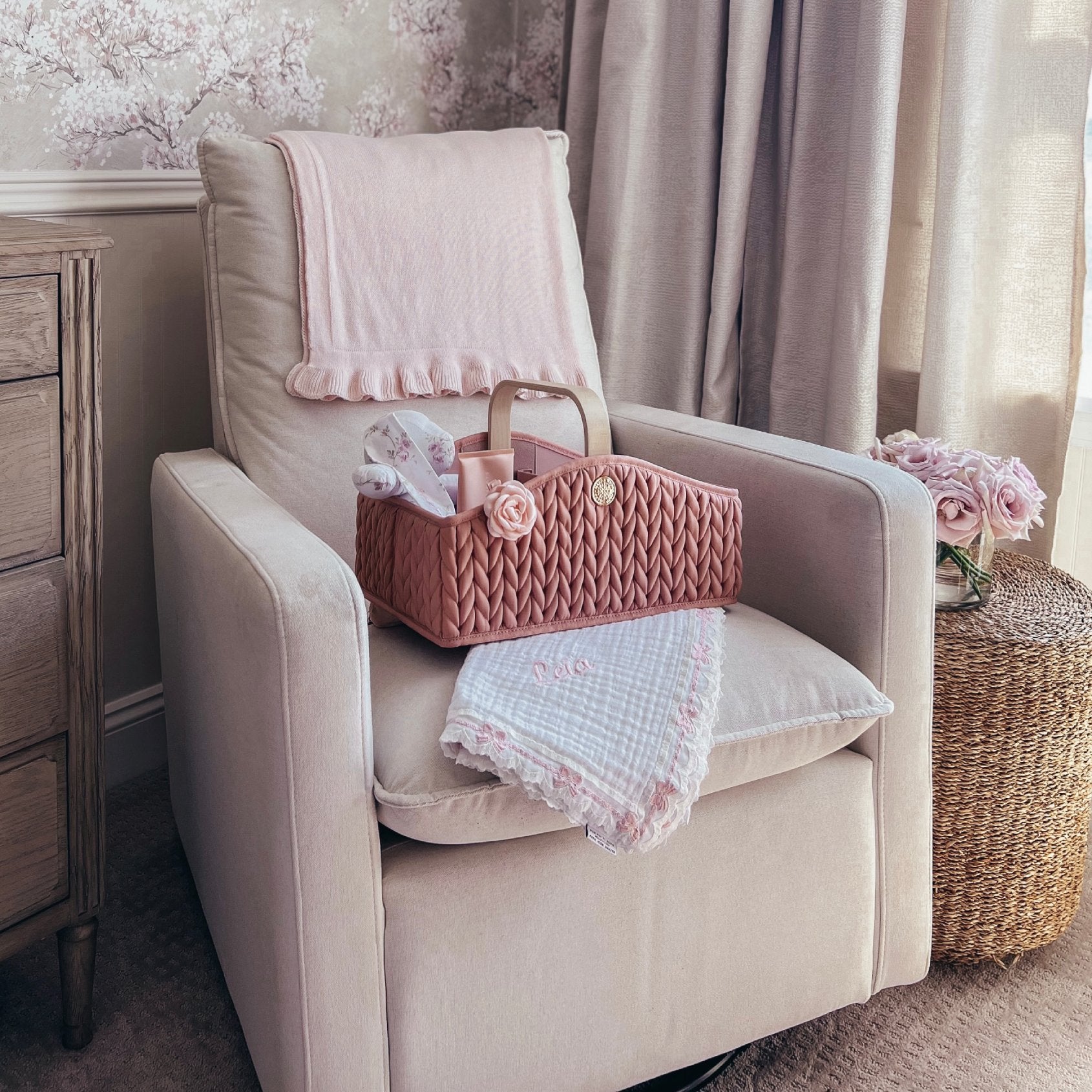 A HAPP Brand Diaper Caddy in Rose sitting on a beige armchair, styled with pink baby blankets and accessories, situated in a chic neutral-themed nursery.