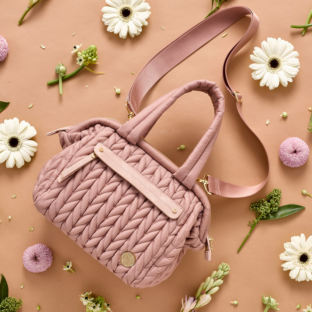 Structured purse-style mini diaper bag in Dusty Rose color, showing carry handles and messenger strap.