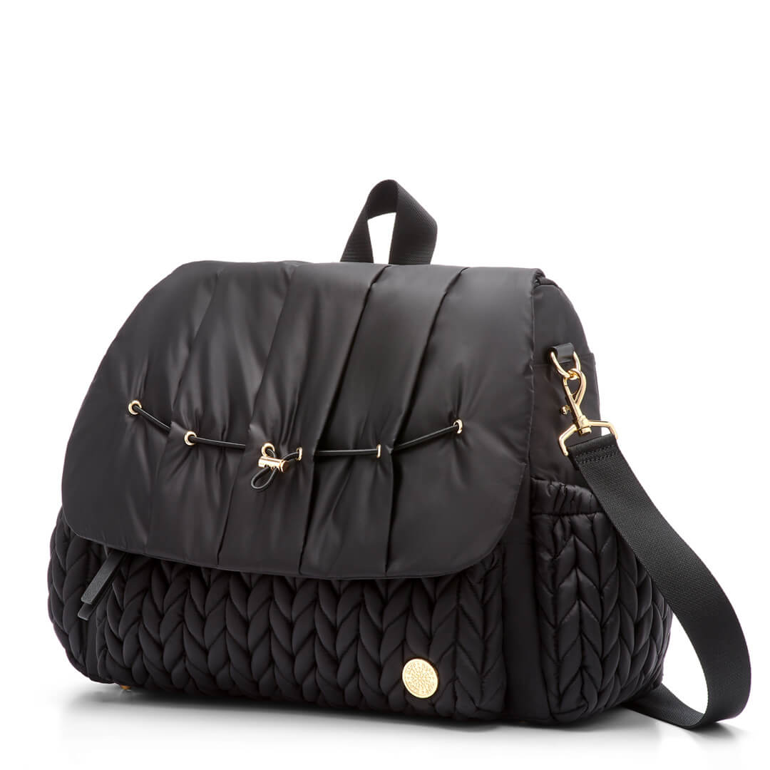 3/4 view of Levy Backpack Black, standing upright and zipped closed, with detachable messenger strap attached. Shows luxe, 3D herringbone fabric, top carry strap, and gold hardware details.