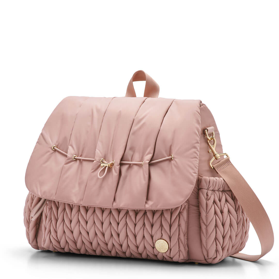 3/4 view of Levy Backpack Dusty Rose, standing upright and zipped closed, with detachable messenger strap attached. Shows luxe, 3D herringbone fabric, top carry strap, and gold hardware details.