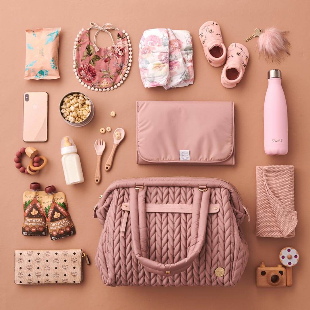 Paige Carryall Rose from the front, with handles folded down, pictured with matching baby and mom items, and with HAPP memory foam changing pad in Rose.