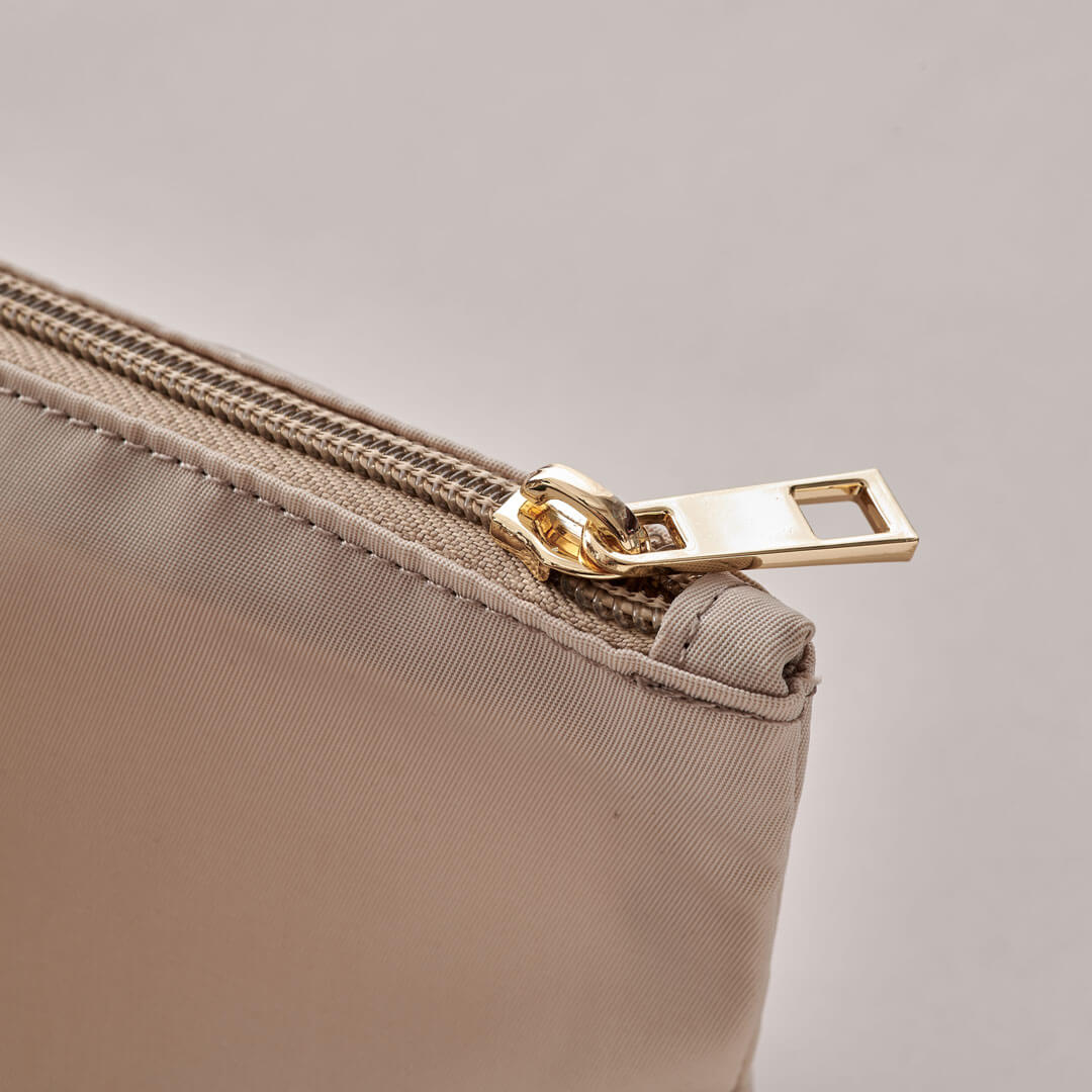 Closeup of gold zipper pull and beige zipper on beige expandable packing pouches.