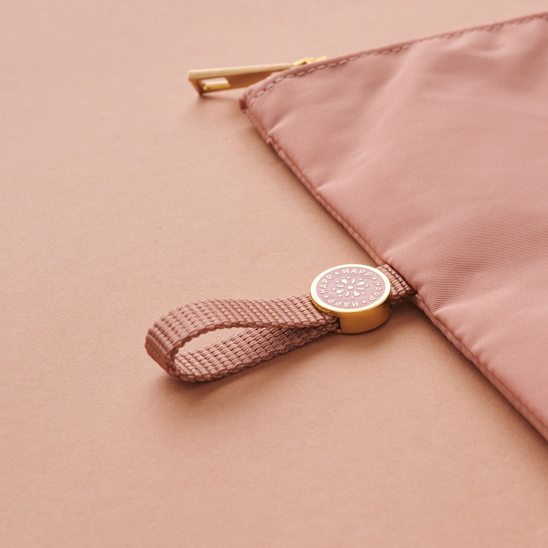 Closeup of the rose pull tab and enamel logo while rose pouch is lying flat on a rose background.