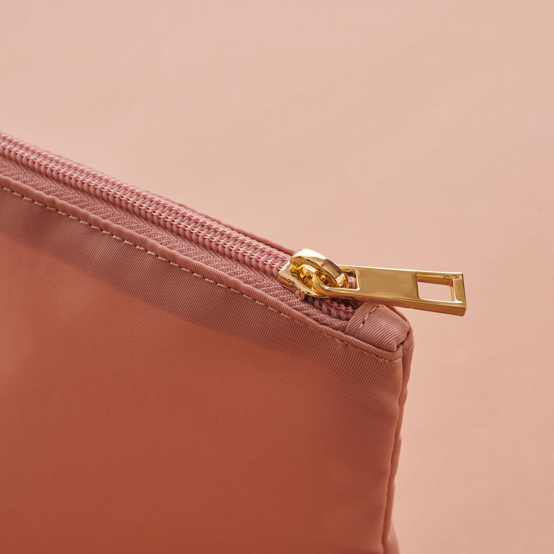 Closeup of gold zipper pull and rose zipper on rose expandable packing pouches.