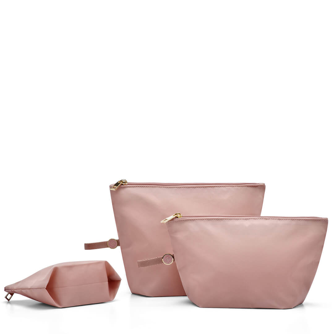 A set of three rose-colored packing pouches of varying sizes, made of a solid material with zipper closures and pull-tab loops, displayed against a white background.