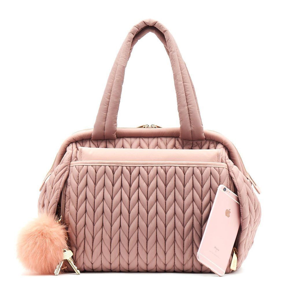 Paige Carryall purse handbag style diaper bag with quilted herringbone nylon in dusty rose blush pink with gold hardware with pink pouf keychain, from the back showing magnet closure changing pad pocket.