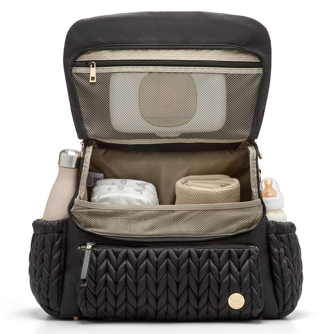 Levy Backpack Black standing upright with the flap open to show the interior mesh pocket and 4 interior pockets. Bottles in the exterior bottle pockets. The bag is lined in Beige fabric.