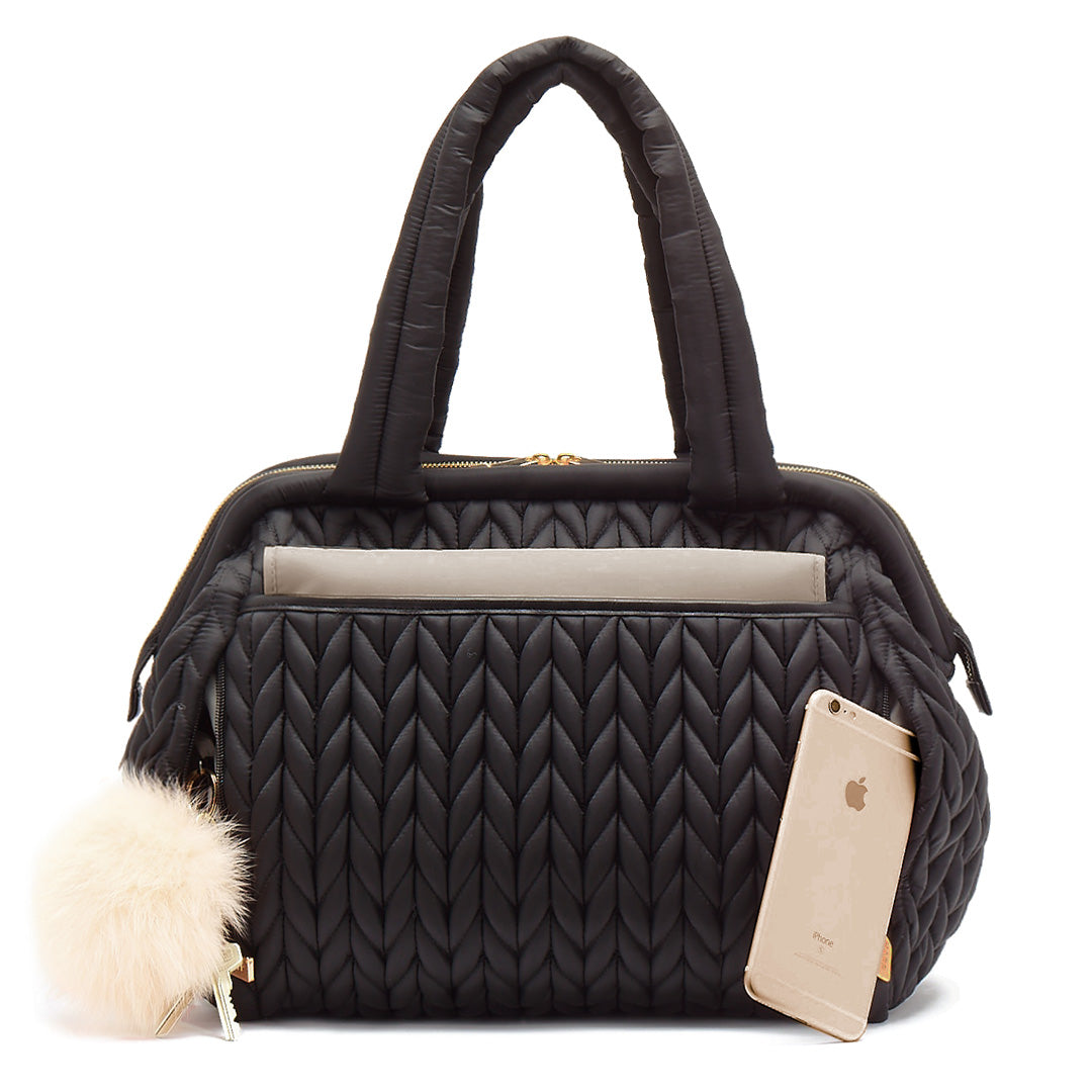 Paige Carryall purse handbag style diaper bag with quilted herringbone nylon in black with gold hardware with ivory pouf keychain, from the back showing magnet closure changing pad pocket.